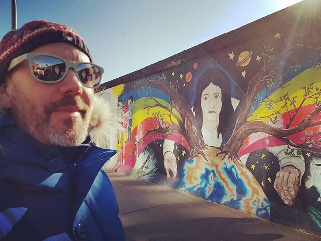 A picture of a dude looking at the Berlin Wall covered in art