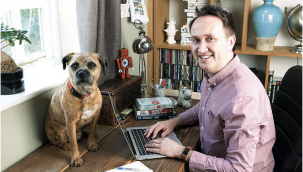 A picture of John Marrs at his desk with his dog