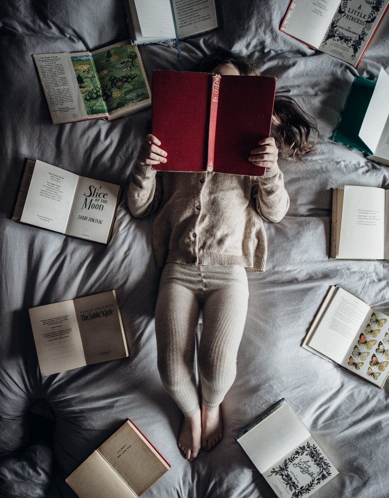A picture of a person laying on a bed with their face in a book